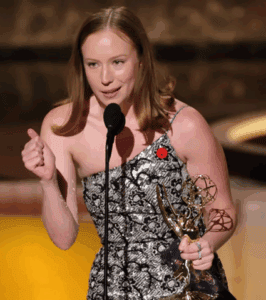 A young woman speaking at an award ceremony, holding a trophy and delivering a speech with confidence.