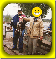 Large catfish caught at a fishing pond, two men holding the fish, outdoor setting, fishing activity, casual clothing, river background, One Citizen Speaking logo in the corner.