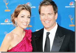 Elegant man and woman at a formal event, smiling in front of a blue background with logos, showcasing style and event photography.