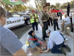 Victim lying on the ground being assisted by bystanders and emergency responders during an outdoor incident with sheriff vehicles in the background.