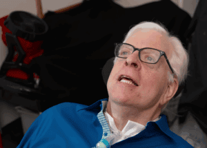 Critically ill man with a tracheostomy speaking at a press conference, emphasizing issues related to healthcare and public safety, highlighting the importance of awareness and advocacy.